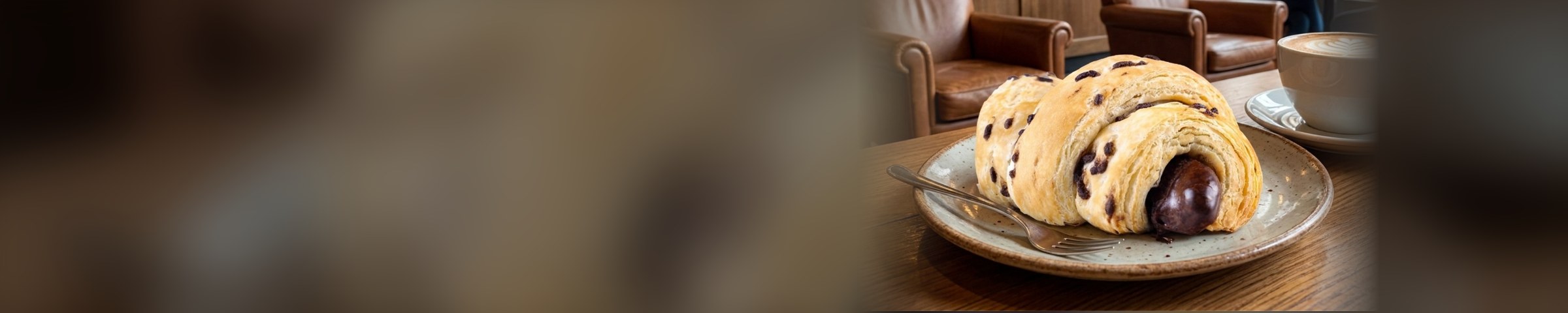 Croissant recheado servido com café no balcão de uma cafeteria