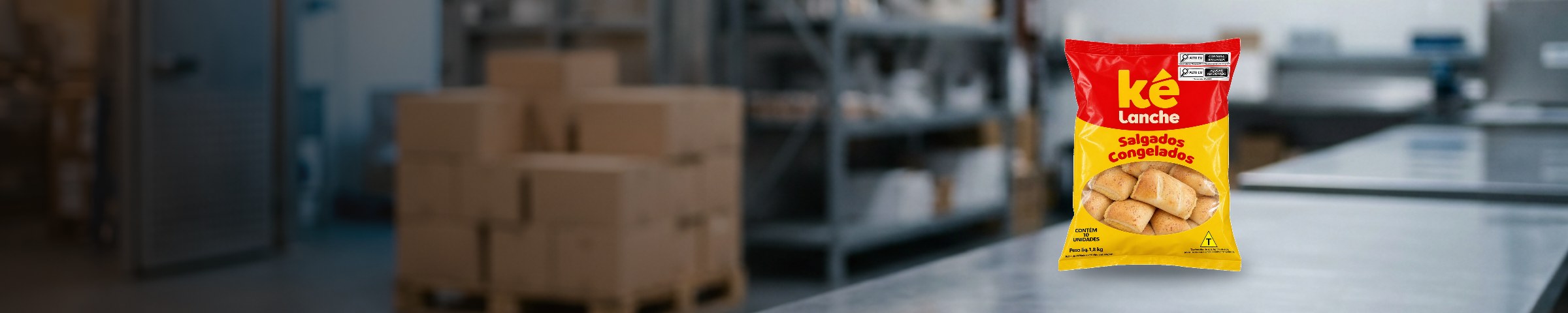 Pacote de 1,8 kg da Ké Lanche sobre a bancada de inox da expedição, com a câmara fria e o palete de caixas desfocados ao fundo