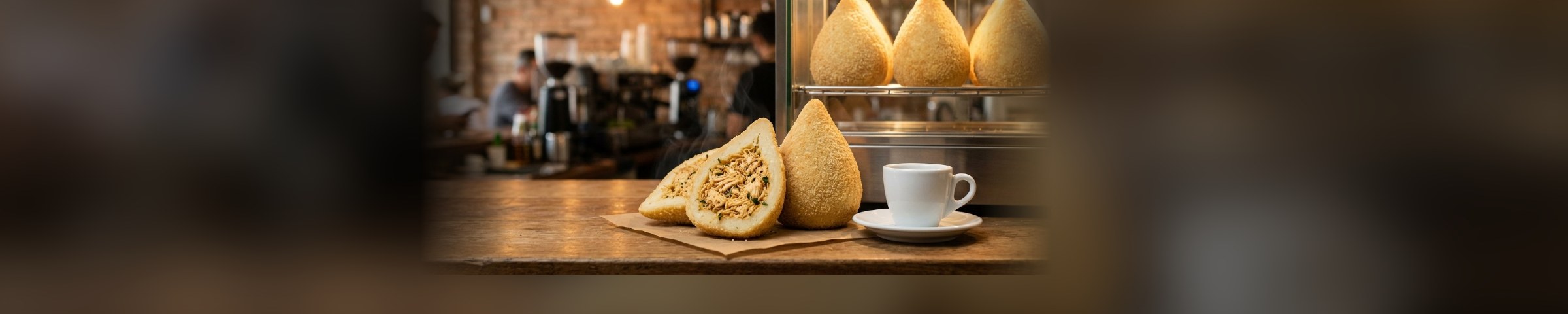 Coxinhas na estufa e, no balcão, uma partida ao meio mostrando o recheio de frango, numa lanchonete em movimento