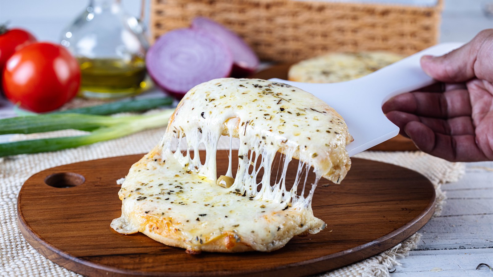 Fatia de pizza sendo levantada da assadeira, com o queijo esticando em fios