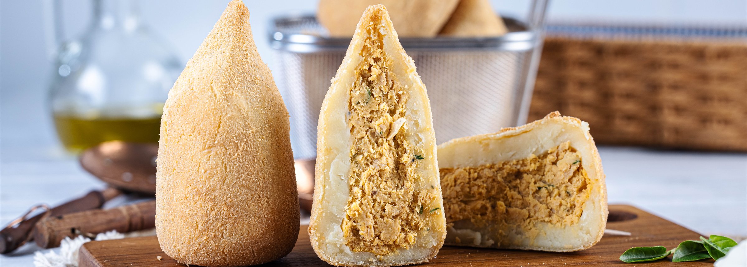 Coxinha partida ao meio mostrando o recheio de frango, ao lado de uma inteira sobre tábua de madeira